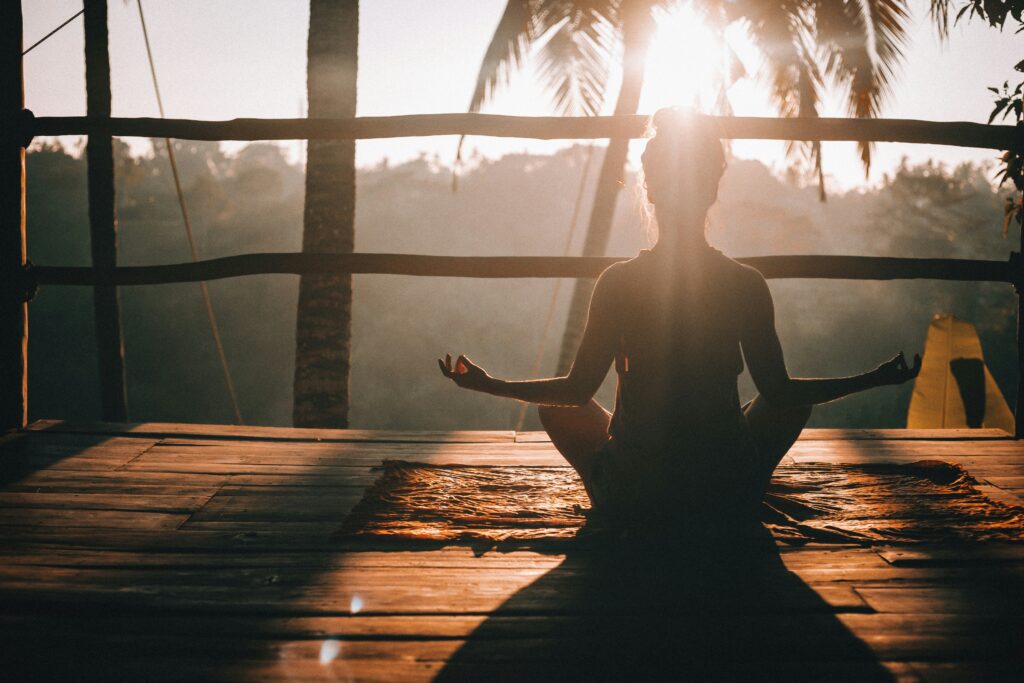 A serene yoga retreat in Bali with participant practicing on a wooden deck surrounded by lush greenery at sunset, offering value wellness travel 2025