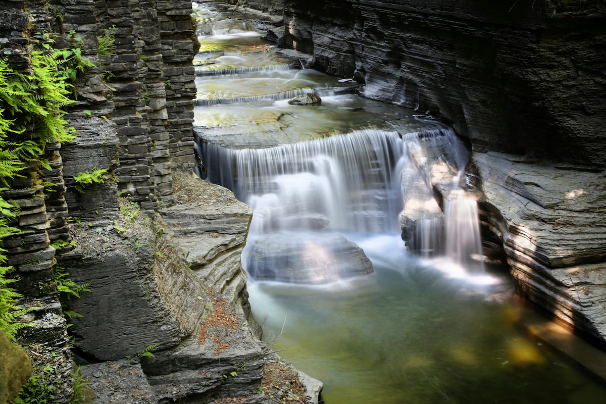 Waterfall cascading through a Finger Lakes gorge trail lined with stone